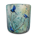 A round ottoman featuring a printed design of  three splendid fairy  blue birds perched on leafy branches against a soft teal and cream background, shown on a plain white studio background.