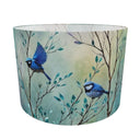 A cylindrical lampshade featuring a printed design of two blue birds perched on delicate branches with soft green and beige foliage against a pale background.
