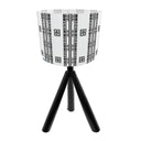 A modern table lamp with a black tripod base and a white drum shade decorated with black geometric tribal patterns.