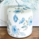 White round velour fabric ottoman with blue hibiscus pattern. 