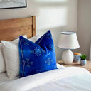 Bedroom with wooden headboard, cobalt blue velvet cushion and white pillows, and a lamp on a nightstand.