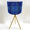 A table lamp with a cobalt blue cylindrical shade featuring a light blue snowflake pattern, supported by three slim gold metal legs lamp stand  on a white background.