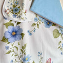 A close-up of a white baby blanket with a delicate blue, green, and pink floral print, with the light blue blanket back folded back on top of the blanket.