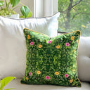 Green floral-patterned pillow on a white couch with a window and plants in the background. 
