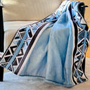 A light blue velvet throw blanket with a black, white, and light blue geometric pattern draped over a beige armchair.