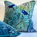 Teal Decorative pillow with blue birds on branches on a white textured surface. 