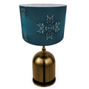 A table lamp with a metallic gold dome-shaped base and a dark teal drum shade decorated with white snowflake patterns, shown against a plain white background.