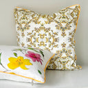 Two decorative throw pillows on a white surface against a light gray wall. The taller pillow has an intricate yellow, black floral damask pattern on a white background, while the shorter pillow in front features a white background with a large yellow lily and pink flower print, finished with yellow piping.