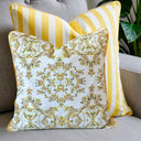 Two decorative throw pillows on a gray sofa. The front pillow has a white background with a yellow and black floral damask pattern, while the rear pillow has bold yellow and white vertical stripes.