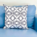 A square throw pillow with a white background and a black symmetrical stirlingia floral pattern, resting on a light blue leather sofa.